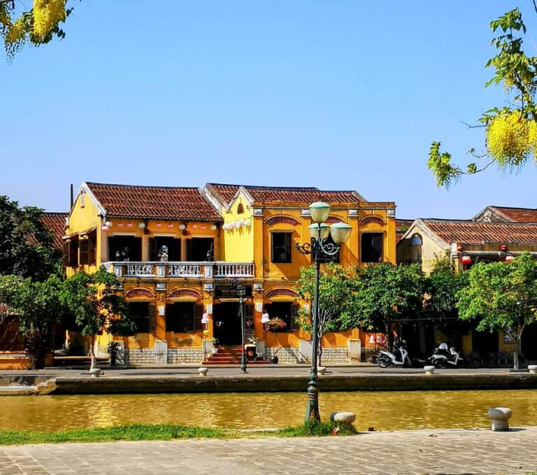 A yellow colonial style, two-storey building, sits on the banks of the river in Hoi An, Vietnam