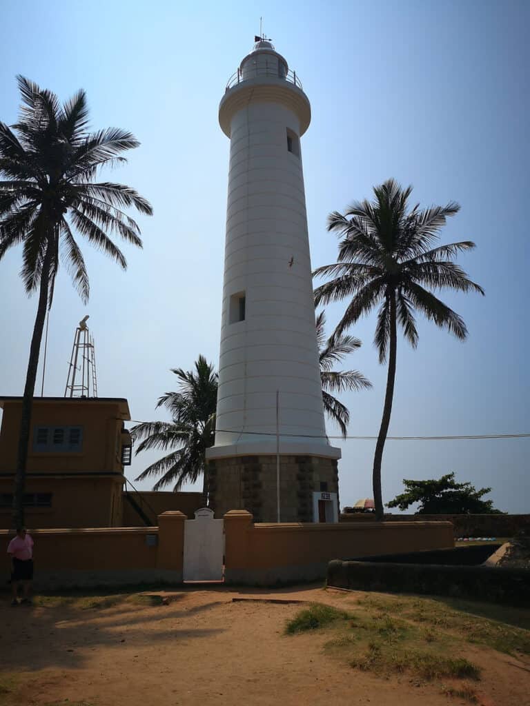 A wite lighthouse is framed by two palm trees in Galle Fort, Sri Lanka