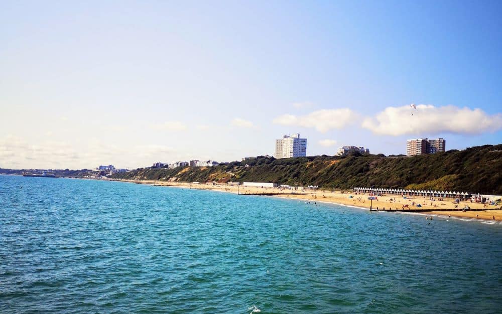 A golden sandy beach sits in front of a grassy hillside and city skyline.