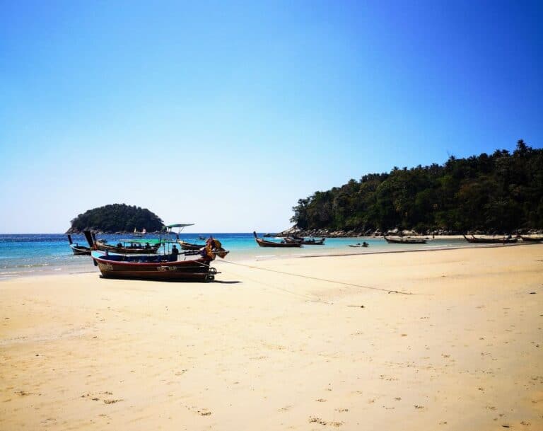 A wooden long tail boat is moored up on a white sandy beach in Phuket, Thailand