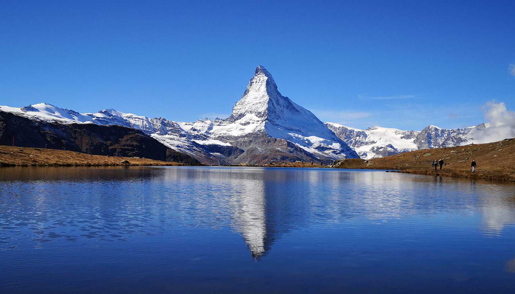 A snow capped mountain peak reflects in a calm lake