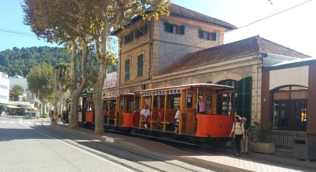 A red vintage tram is stationed in front of a stone building in Port De Soller, Mallorca