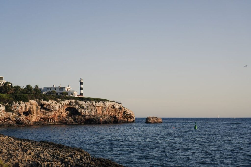 A small lighthouse perches at the edge of a rocky outcrop on the Mallorca Coastline