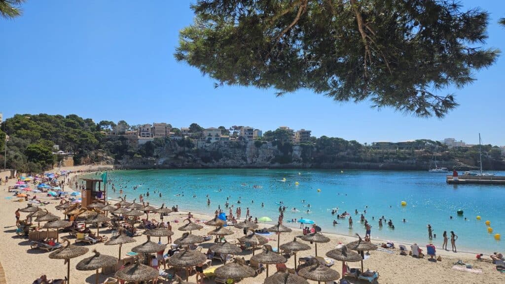 A rocky cove with blue sea and a small sandy beach, lined with straw umbrellas